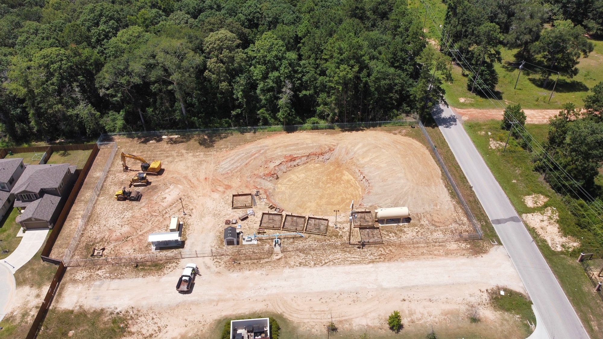 Aerial view of excavation, form assemblies, earthmoving equipment and a wooded site boundary