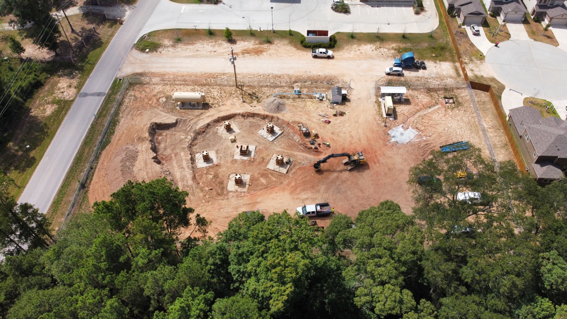 Aerial view of an excavated construction site with prepared concrete foundations and an excavator