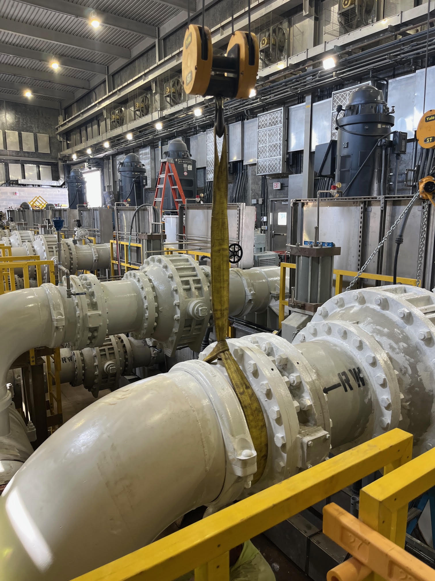 Industrial piping and process equipment surrounded by yellow safety railings in a utility building